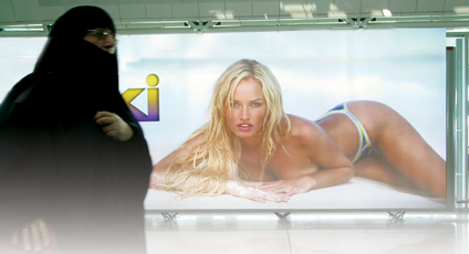 Photographie d'une femme voilée derrière une affiche sexy