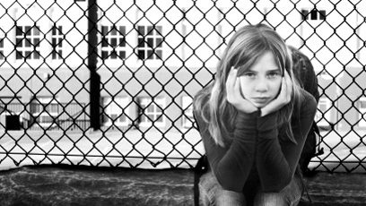 Jeune fille assise devant une clôture.
