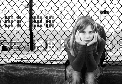 Jeune fille assise devant une clôture.