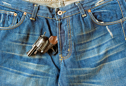 Photographie de jeans avec un fusil qui sort de l'entrejambe