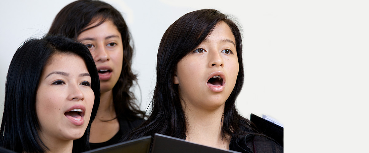 Photographie de trio de jeunes femmes qui chantent.