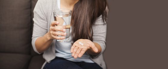 Jeune femme tenant 2 pilules abortives et un verre d'eau.