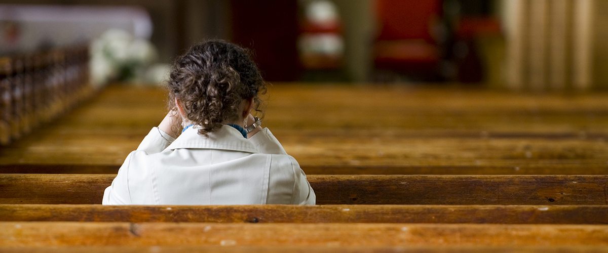 Une jeune femme de dos assise à l'église.