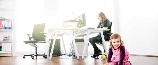 Jeune mère à l'ordinateur avec son enfant qui joue.