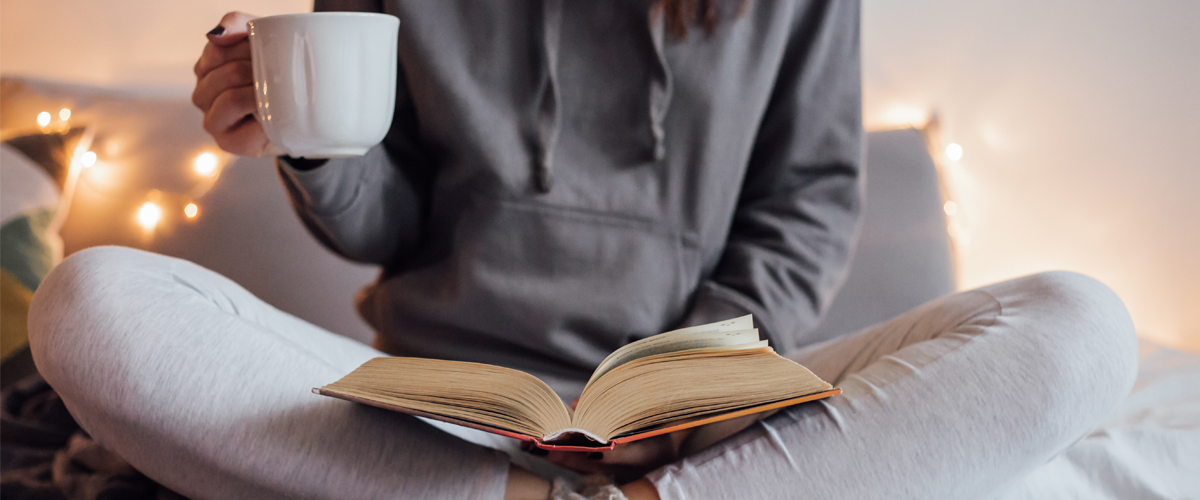 Femme lisant un livre avec sa tasse de café en main.