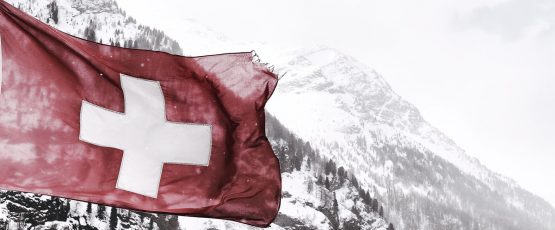 Drapeau de la Suisse flottant à la cime d'une montagne enneigée.